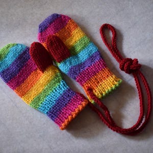Toddler mittens in rainbow color with red thumbs. Presented with string between the mittens to prevent loss. Option for string can be added at no extra cost.