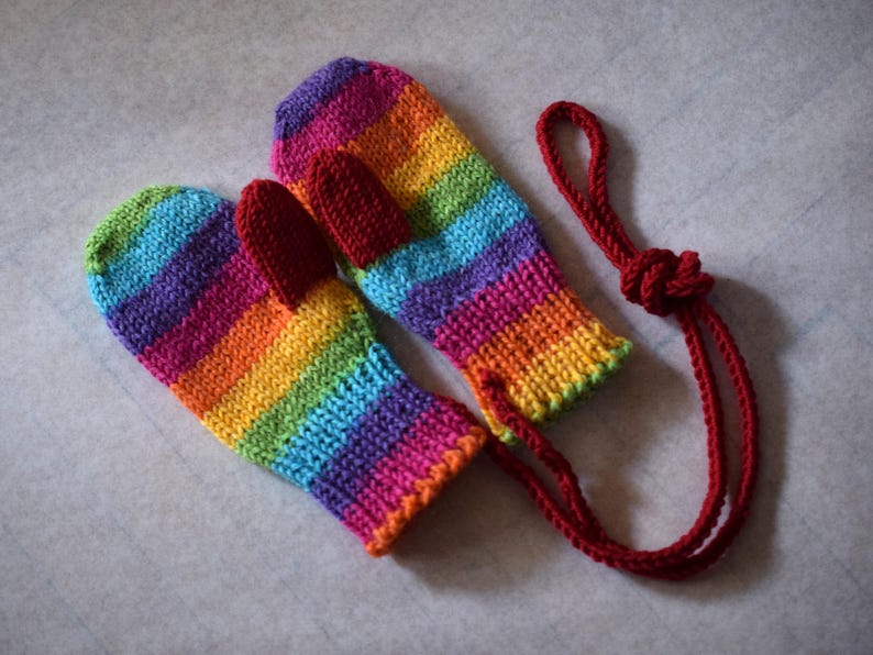 Toddler mittens in rainbow color with red thumbs. Presented with string between the mittens to prevent loss. Option for string can be added at no extra cost.