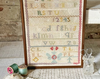 A beautiful antique late 1800’s sampler framed in a wooden frame behind glass