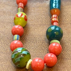 May include: A colorful beaded necklace with red, green, and blue beads. The beads are made of different materials, including glass and wood. The necklace is strung on a clear cord.