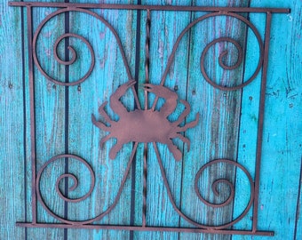 Peut inclure: Une silhouette de crabe en métal brun rouillé fixée à une porte en métal décorative avec des détails enroulés. La porte est montée sur un mur en bois bleu sarcelle.