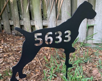 May include: Black metal silhouette of a dog with the house number 5633 cut out. The silhouette is mounted on a metal stake and is placed in the ground.
