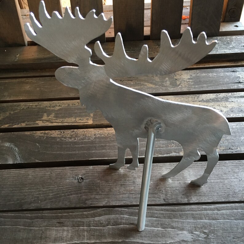 May include: A silver metal moose silhouette with large antlers. The moose is standing on a metal rod that is inserted into the ground.