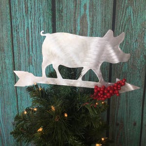 May include: A silver metal pig silhouette Christmas tree topper with a red berry sprig attached to the arrow.