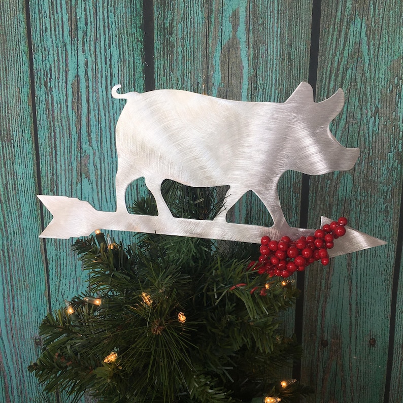 May include: A silver metal pig silhouette Christmas tree topper with a red berry sprig attached to the arrow.