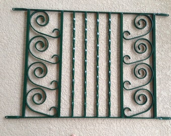 Peut inclure: Une grille de sécurité de fenêtre en métal vert avec un motif de volutes décoratif.