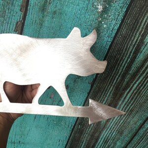 May include: A metal pig silhouette wind vane with an arrow pointing to the right. The pig is made of brushed metal and has a shiny finish.