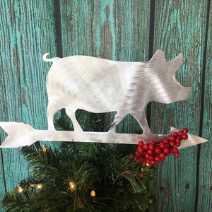May include: A silver metal pig silhouette Christmas tree topper with a red berry sprig and an arrow pointing to the right.