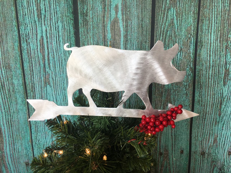 May include: A silver metal pig silhouette Christmas tree topper with a red berry sprig and an arrow pointing to the right.