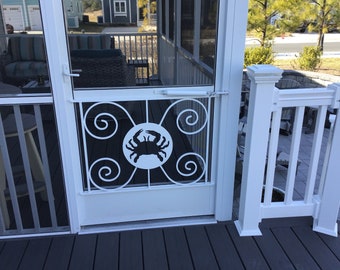 Peut inclure: Porte moustiquaire blanche avec une porte en métal blanc ornée d'une silhouette noire de crabe dans un cercle. La porte a un motif de volutes décoratif.