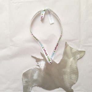 May include: A silver metal ornament shaped like a dog with a white ribbon tied around it. The ribbon has the text "Merry & Bright" printed on it.