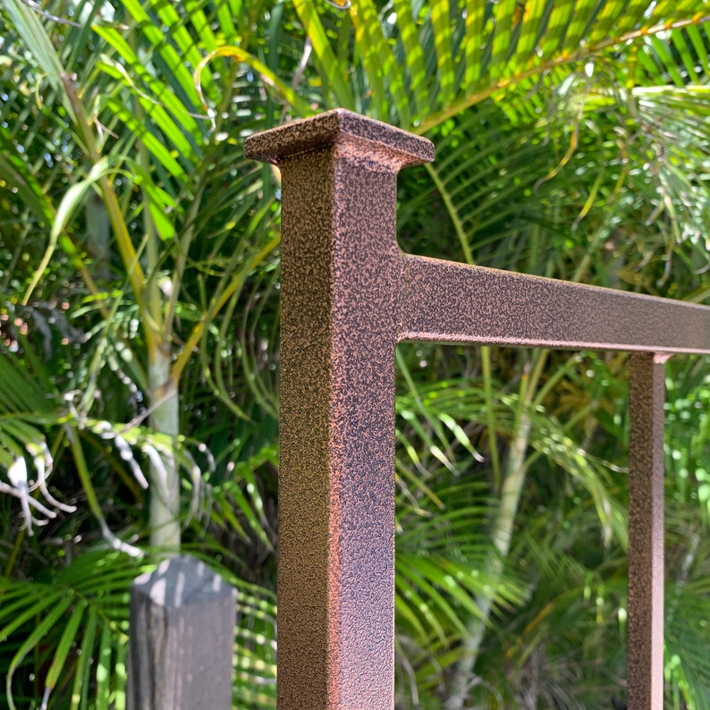 May include: Close-up of a bronze-coloured metal fence post with a textured finish. The post is square and has a flat top.