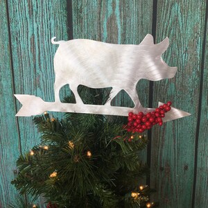 May include: A silver pig silhouette Christmas tree topper with a red berry garland and an arrow.