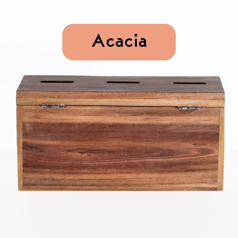 Puede incluir: Una caja de madera con tapa abatible, hecha de madera de acacia. La caja tiene cuatro ranuras en la parte superior.