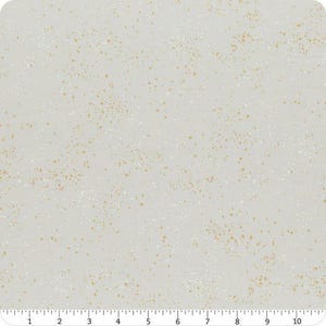 May include: A light gray fabric featuring a speckled pattern of small gold and white dots across the surface. A ruler is visible along the bottom edge, showing a measurement scale of 10 inches for the width of the textile material.