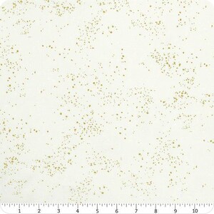 Peut inclure: Un tissu blanc présentant un motif dispersé de petites taches métalliques dorées sur toute la surface. Une règle est visible sur le bord inférieur, affichant des mesures en centimètres de 1 à 10, indiquant l'échelle du motif textile.