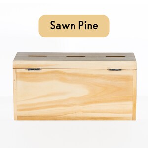 Puede incluir: Una caja de madera con tapa con bisagras y tres ranuras en la parte superior. La caja est&aacute; hecha de madera de pino aserrada y tiene un acabado de madera natural. El texto "Sawn Pine" est&aacute; impreso en una etiqueta amarilla.