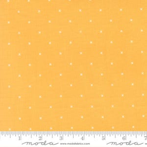 May include: A bright yellow fabric featuring a repeating pattern of small white cross symbols. A white ruler is visible at the bottom edge, showing a measurement scale of 7 inches across the width of the textile material.