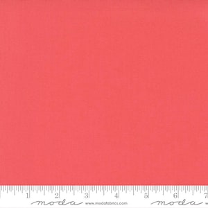 May include: A solid coral-coloured fabric swatch featuring a fine woven texture. A white ruler is positioned along the bottom edge, showing measurements in centimetres from 0 to 18. The text "moda" and "www.modafabrics.com" are printed on the ruler.
