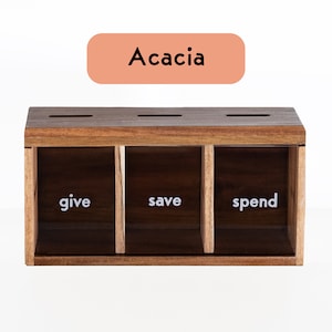 Puede incluir: Una caja de madera con tres compartimentos etiquetados como "give", "save" y "spend". La caja est&aacute; hecha de madera de acacia.
