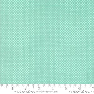 May include: A light mint green fabric featuring a repeating pattern of tiny white dots. A white ruler is visible at the bottom edge, showing measurements in inches from 0 to 7. The text "moda" and "www.modafabrics.com" is printed on the ruler.
