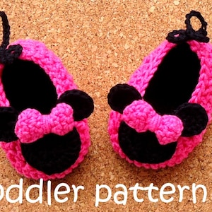 May include: A pair of handmade pink and black crochet baby shoes. The shoes feature a Minnie Mouse design with a bow and ears. The text "toddler pattern" is visible in white.