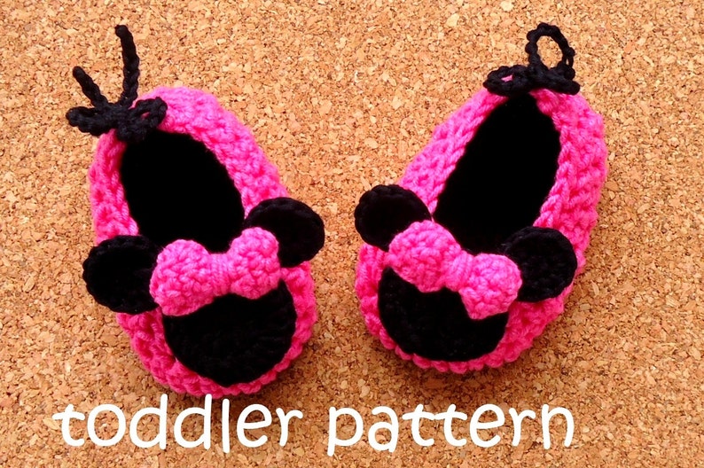 May include: A pair of handmade pink and black crochet baby shoes. The shoes feature a Minnie Mouse design with a bow and ears. The text "toddler pattern" is visible in white.