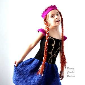 May include: A girl wearing a blue and black crochet dress with a pink crown and long brown and white braids. The dress has a gold design on the bodice.  Beauty Crochet Pattern.