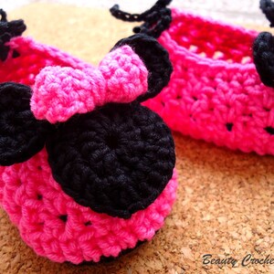 May include: Two handmade, bright pink crochet baby shoes with black bows. The shoes are in a basket weave pattern. The text "Beauty Crochet Pattern" is in the bottom right corner.