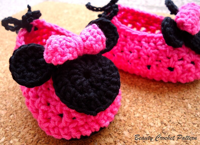 May include: Two handmade, bright pink crochet baby shoes with black bows. The shoes are in a basket weave pattern. The text "Beauty Crochet Pattern" is in the bottom right corner.