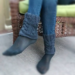 May include: A pair of blue denim jeans with dark blue knitted leg warmers. The leg warmers have a cable knit pattern.