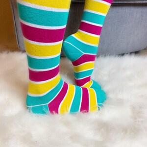 Peut inclure: Chaussettes hautes &agrave; rayures horizontales jaunes, turquoise et magenta. Les chaussettes sont pos&eacute;es sur une surface blanche et duveteuse. Accessoire de mode color&eacute; et amusant.