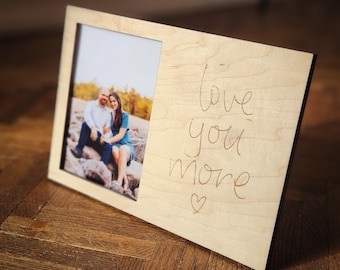 May include: A wooden picture frame with a photo of a couple in the frame. The frame has the words "Love you more" engraved on it.