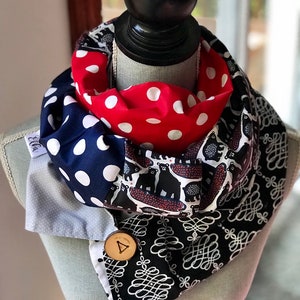 May include: An infinity scarf with a variety of patterns, displayed on a mannequin. The scarf includes navy blue with white spots, red with white spots, and a black and white bear print. A wooden button fastens the scarf.