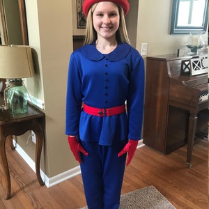 May include: A young person wearing a blue outfit with a red belt and red gloves. They are also wearing a red hat with a brim.