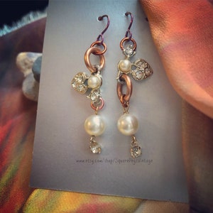 May include: A pair of dangle earrings with a copper chain, white pearls, and clear rhinestones. The earrings have a vintage style.