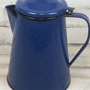 May include: A blue speckled enamelware coffee pot with a lid and handle. The pot has a classic design, with a spout for pouring. The handle is a simple, curved shape. The pot is likely used for camping or outdoor activities.