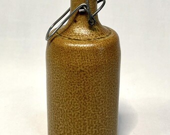May include: A brown stoneware bottle with a textured surface and a swing-top closure featuring a white ceramic stopper and a metal wire bail. The lower portion of the bottle is embossed with the text 0,7l and MIK-M.