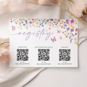 May include: A white card with a floral border and the word "registry" in purple script.  The card lists three online retailers: Amazon, Anthropologie, and Target. Each retailer has a QR code and a link to their registry.
