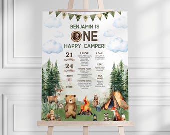 Puede incluir: Un póster imprimible de estilo acuarela para una fiesta de primer cumpleaños con temática de bosque. El póster presenta una foto de un bebé, una fogata, animales y el texto "¡Benjamin tiene un año, feliz campista!" junto con detalles sobre la edad del bebé, sus comidas favoritas y canciones.