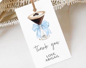 May include: A white thank you tag with a blue ribbon tied around a glass of coffee. The text on the tag reads "Thank you, Love, Abigail".