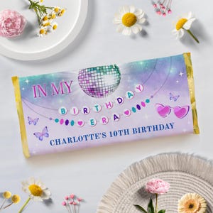 Puede incluir: Un envoltorio de barra de chocolate morado, azul y blanco con una bola de discoteca, mariposas y el texto "In My Birthday" y "Charlotte's 10th Birthday".