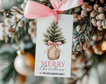 May include: A white gift tag with a watercolor illustration of a small potted Christmas tree with a pink ribbon. The text "Merry Christmas" is written in pink script with a heart and the text "THE WILLIAMSON FAMILY" below.