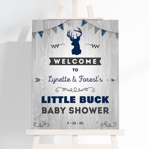 May include: Welcome to Lynette & Forest's Little Buck Baby Shower sign with a gray woodgrain background, blue and white plaid bunting, a silhouette of a deer head, and the date 9.28.XX.