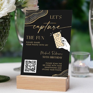 May include: Black and gold birthday party sign with a QR code. The sign says "Let's capture the fun. Please share your photo with us! Michael Robison's 50th Birthday. Please scan the QR code with your smartphone and upload your photo."