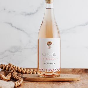 Peut inclure: Une bouteille de vin ros&eacute; avec une &eacute;tiquette &agrave; motif floral qui dit "Cheers to the future" et "Mrs. Hutchinson".