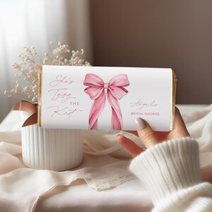 Op de afbeelding: Een witte chocoladeverpakking met een roze strik en de tekst "She's tying the knot" en "Abigail's Bridal Shower".