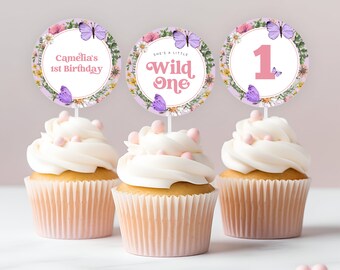 May include: Three cupcakes with pink frosting and purple and white butterfly themed cupcake toppers. The toppers say "Camelia's 1st Birthday", "She's a Little Wild One", and "1".