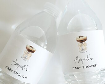 May include: Two clear plastic water bottles with white labels. The labels feature a hand-drawn illustration of a cocktail glass with a brown and white drink, topped with coffee beans. The text on the labels reads "Abigail's Baby Shower".