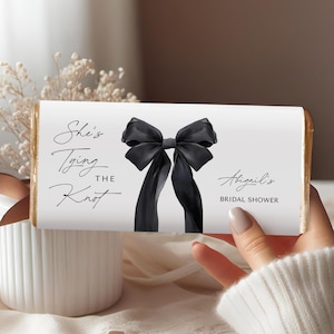 Op de afbeelding: Witte chocolade reep met een zwarte strik en de tekst "She's Tying the Knot" en "Abigail's Bridal Shower".